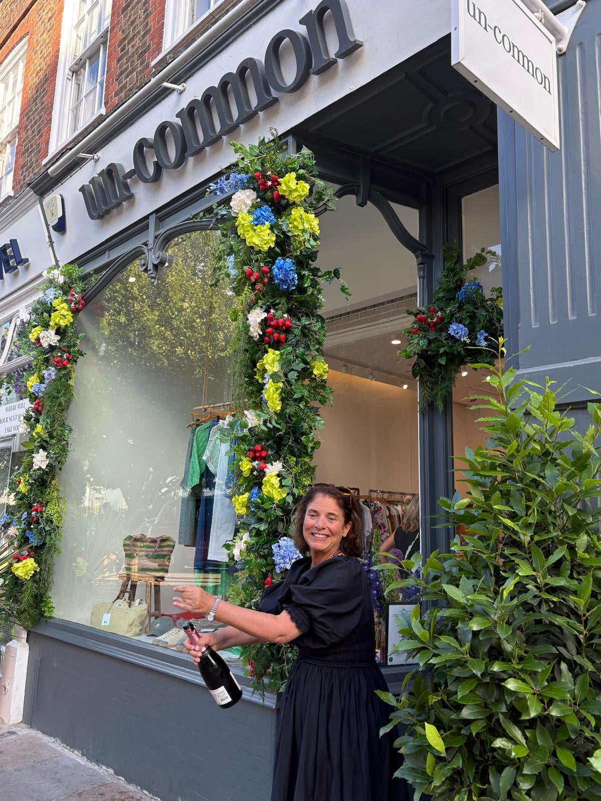 Kate from un-common, a Wimbledon-based boutique, opening a bottle of fizzy wine in front of the new storefront.