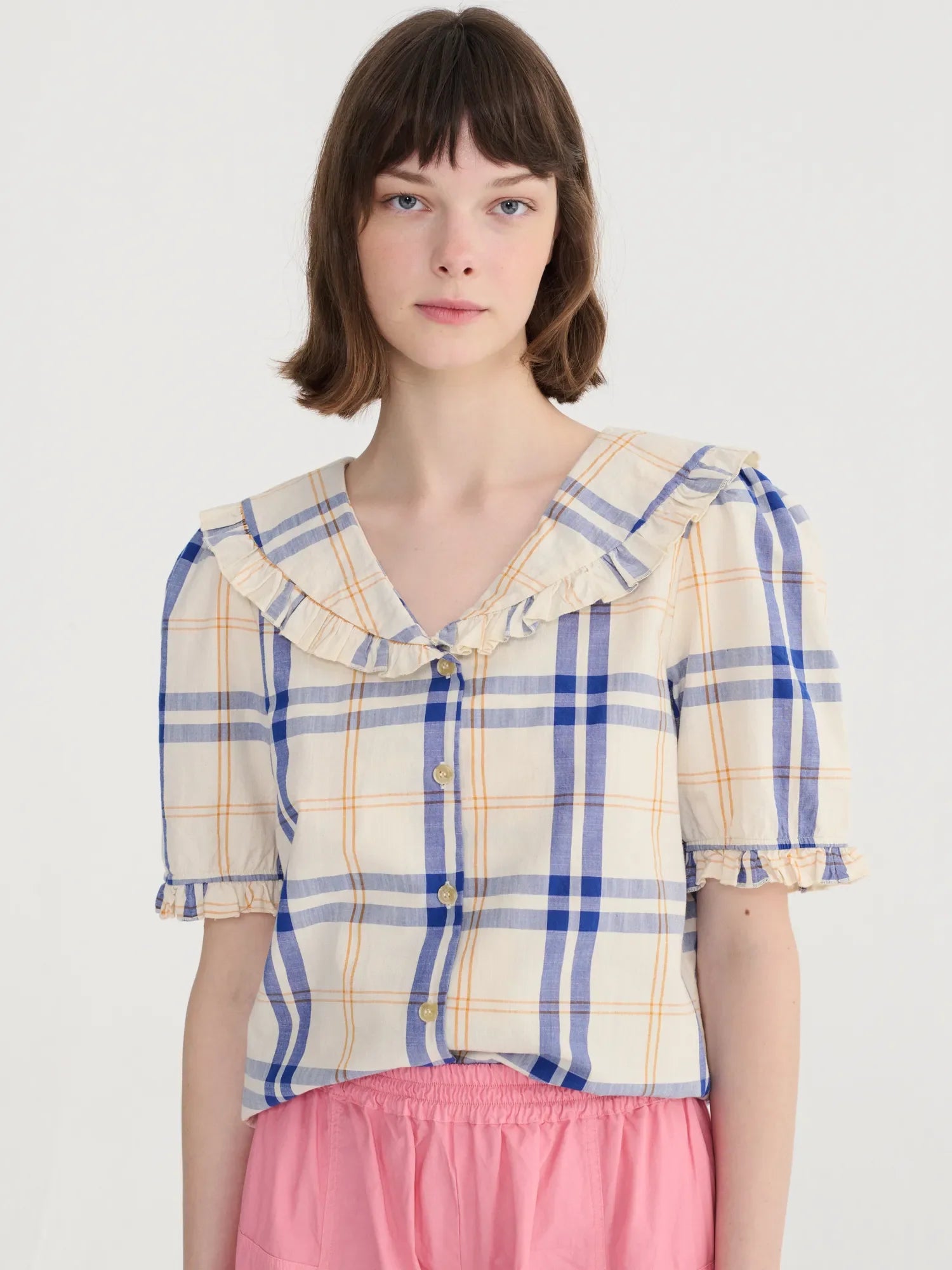Woman wearing a plaid shirt with ruffled collar on a white background